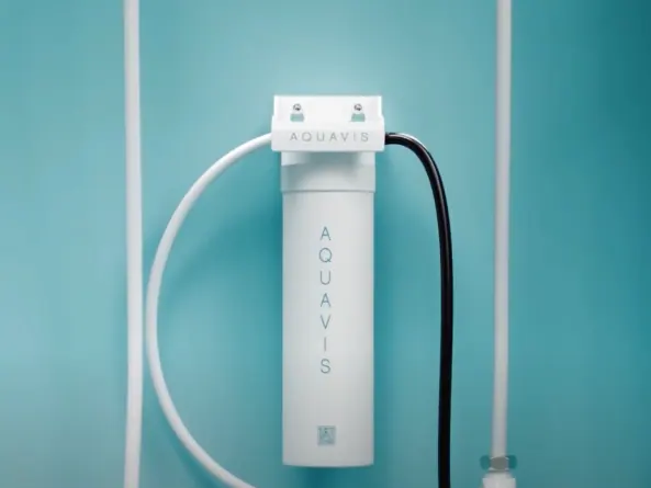 An Aquavis under-sink filter cartridge mounted on a teal wall with white and black supply lines.