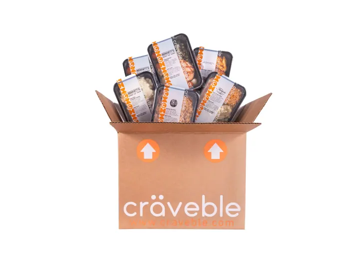 An open Craveble shipping box packed with sealed, labeled meal trays, on white.